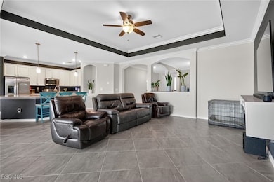 Living room with a raised ceiling, ornamental molding, light tile patterned floors, ceiling fan, and recessed lighting
