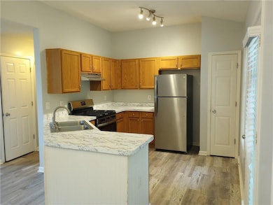 Kitchen with stainless steel appliances, light countertops, brown cabinets, a peninsula, and light wood-style flooring