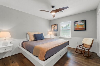 Cozy bedroom with a modern ceiling fan and warm wooden flooring. It features a comfortable bed, soft lighting from bedside lamps, and a window letting in natural light.