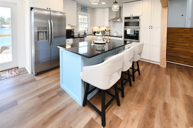 Kitchen featuring appliances with stainless steel finishes, wall chimney exhaust hood, light wood finished floors, dark countertops, and tasteful backsplash