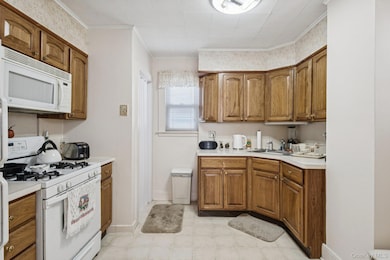 Kitchen featuring white appliances, brown cabinets, light countertops, crown molding, and wallpapered walls