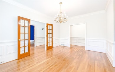 Unfurnished dining area with ornamental molding, a chandelier, a decorative wall, french doors, and light wood-style floors