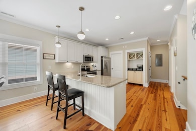 Kitchen featuring appliances with stainless steel finishes, a peninsula, crown molding, a kitchen bar, and light wood-style flooring
