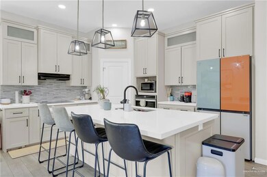 Kitchen with glass insert cabinets, stainless steel appliances, a kitchen breakfast bar, decorative backsplash, and an island with sink
