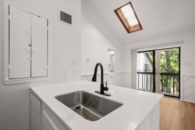 Kitchen featuring a skylight, light wood finished floors, vaulted ceiling, light stone counters, and wainscoting
