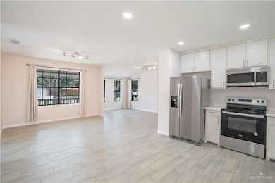 Kitchen featuring stainless steel appliances, light countertops, open floor plan, light wood finished floors, and white cabinets