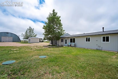 Rear view of property with an outdoor structure, a lawn, and dirt driveway
