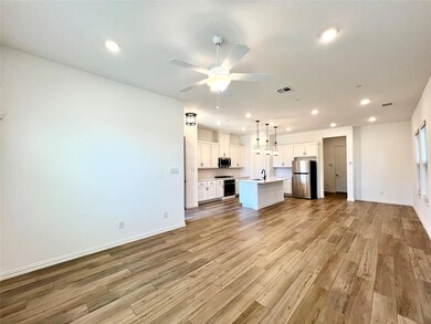 Kitchen featuring light wood-type flooring, an island with sink, open floor plan, stainless steel appliances, and white cabinets