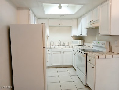 Kitchen with white appliances, tile counters, and