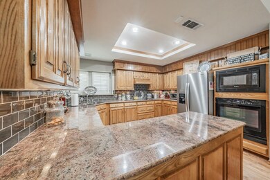 Kitchen featuring black appliances, light wood-type flooring, light stone countertops, kitchen peninsula, and backsplash