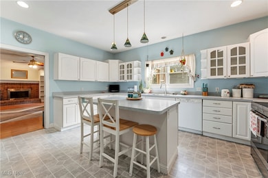 Kitchen featuring a kitchen bar, glass insert cabinets, hanging light fixtures, a brick fireplace, and recessed lighting