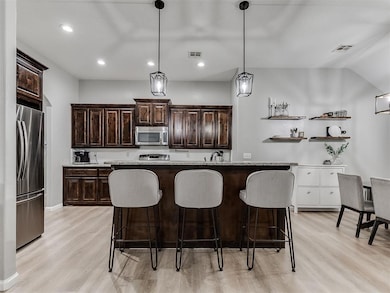 Kitchen featuring appliances with stainless steel finishes, light wood-style flooring, dark brown cabinets, a kitchen bar, and recessed lighting