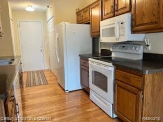 Kitchen with white appliances, dark countertops, brown cabinets, and light wood-type flooring