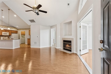 Unfurnished living room featuring light wood finished floors, a tiled fireplace, high vaulted ceiling, a ceiling fan, and washer / clothes dryer