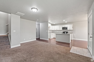 Kitchen featuring dark colored carpet, white cabinets, open floor plan, appliances with stainless steel finishes, and a center island with sink