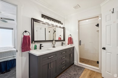 Ensuite bathroom with double vanity, crown molding, a shower stall, and light wood-style floors