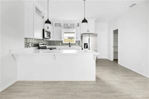 Kitchen featuring light countertops, decorative backsplash, appliances with stainless steel finishes, a peninsula, and white cabinetry