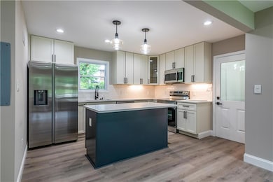 Kitchen with stainless steel appliances, decorative backsplash, light wood finished floors, light countertops, and recessed lighting