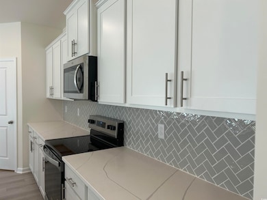 Kitchen featuring appliances with stainless steel finishes, decorative backsplash, white cabinets, and light stone countertops