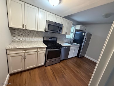 Kitchen with appliances with stainless steel finishes, tasteful backsplash, dark wood-style floors, light stone countertops, and white cabinetry