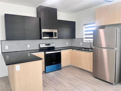Kitchen with a peninsula, stainless steel appliances, dark countertops, light brown cabinets, and a sink