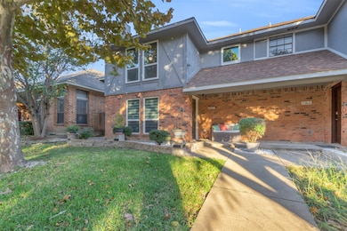 View of front of property featuring brick siding, a front lawn, roof with shingles, and stucco siding