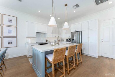 Kitchen featuring ornamental molding, stainless steel fridge, white cabinetry, a kitchen island with sink, and a kitchen breakfast bar