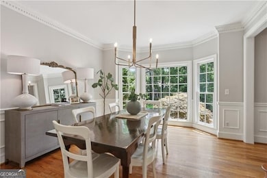 Dining space featuring a chandelier, ornamental molding, healthy amount of natural light, wood finished floors, and a decorative wall