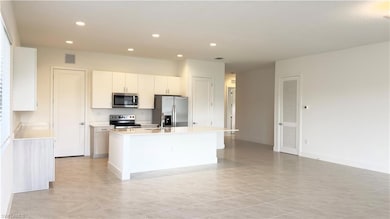 Kitchen featuring white cabinets, stainless steel appliances, recessed lighting, an island with sink, and light tile patterned floors