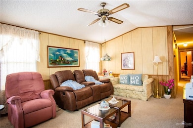 Carpeted living room with wooden walls, a textured ceiling, vaulted ceiling, ceiling fan, and ornamental molding
