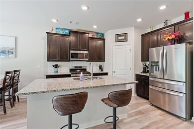 Kitchen featuring appliances with stainless steel finishes, dark brown cabinetry, light wood-style flooring, an island with sink, and recessed lighting