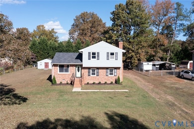 Split level home featuring a detached carport, a chimney, brick siding, and view of wooded area