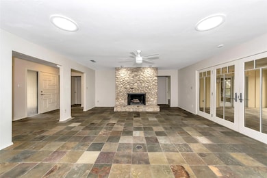 Unfurnished living room featuring stone tile flooring, ceiling fan, french doors, and a stone fireplace