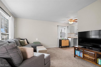 Living area with ceiling fan, light carpet, and light wood finished floors