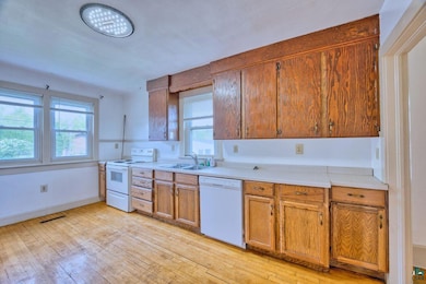 Kitchen with white appliances, a sink, light wood-style flooring, and light countertops