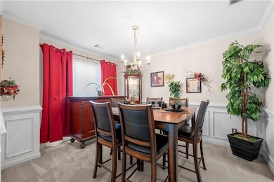 Dining room with a chandelier, light carpet, ornamental molding, and wainscoting