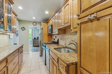 Kitchen featuring a sink, backsplash, stainless steel appliances, light stone countertops, and glass insert cabinets