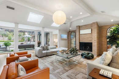 Upon entering, you are immediately drawn to the expansive floor-to-ceiling picture windows, which span the back of the living room, flooding the space with natural light and offering serene views of the backyard and patio. Vaulted ceiling with wood beams, recessed lighting, and skylights create an open, inviting ambiance.