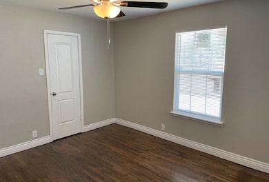 Spare room with dark wood-style flooring, a ceiling fan, and baseboards