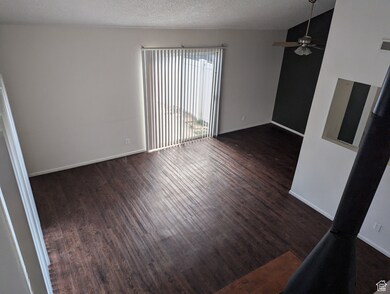 Empty room featuring a textured ceiling, dark wood-style flooring, and a ceiling fan
