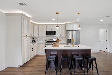 Kitchen featuring decorative light fixtures, stainless steel appliances, tasteful backsplash, dark wood-style flooring, and a kitchen island with sink