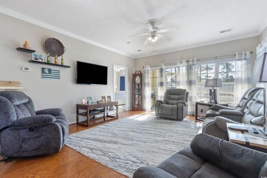 Living area featuring a ceiling fan, a textured ceiling, wood finished floors, crown molding, and baseboards