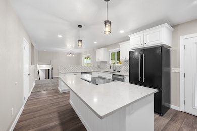 Kitchen with white cabinets, freestanding refrigerator, a kitchen island, decorative backsplash, and dark wood-type flooring