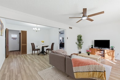 Living room featuring a ceiling fan, light wood-type flooring, ornamental molding, a textured ceiling, and a chandelier