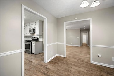 Kitchen featuring stainless steel appliances, wood finished floors, a textured ceiling, and white cabinets