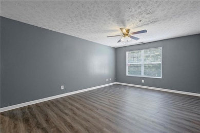 Unfurnished room featuring dark wood-style floors, a ceiling fan, and a textured ceiling