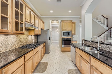 Kitchen featuring backsplash, ornamental molding, appliances with stainless steel finishes, light tile patterned flooring, and dark stone counters