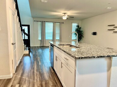 Kitchen featuring white cabinets, dark wood-type flooring, light stone countertops, a center island with sink, and ceiling fan