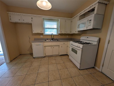 Kitchen with white appliances, light countertops, white cabinetry, and light tile patterned flooring