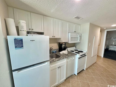 Kitchen featuring white appliances, light tile patterned floors, white cabinetry, a textured ceiling, and stone countertops